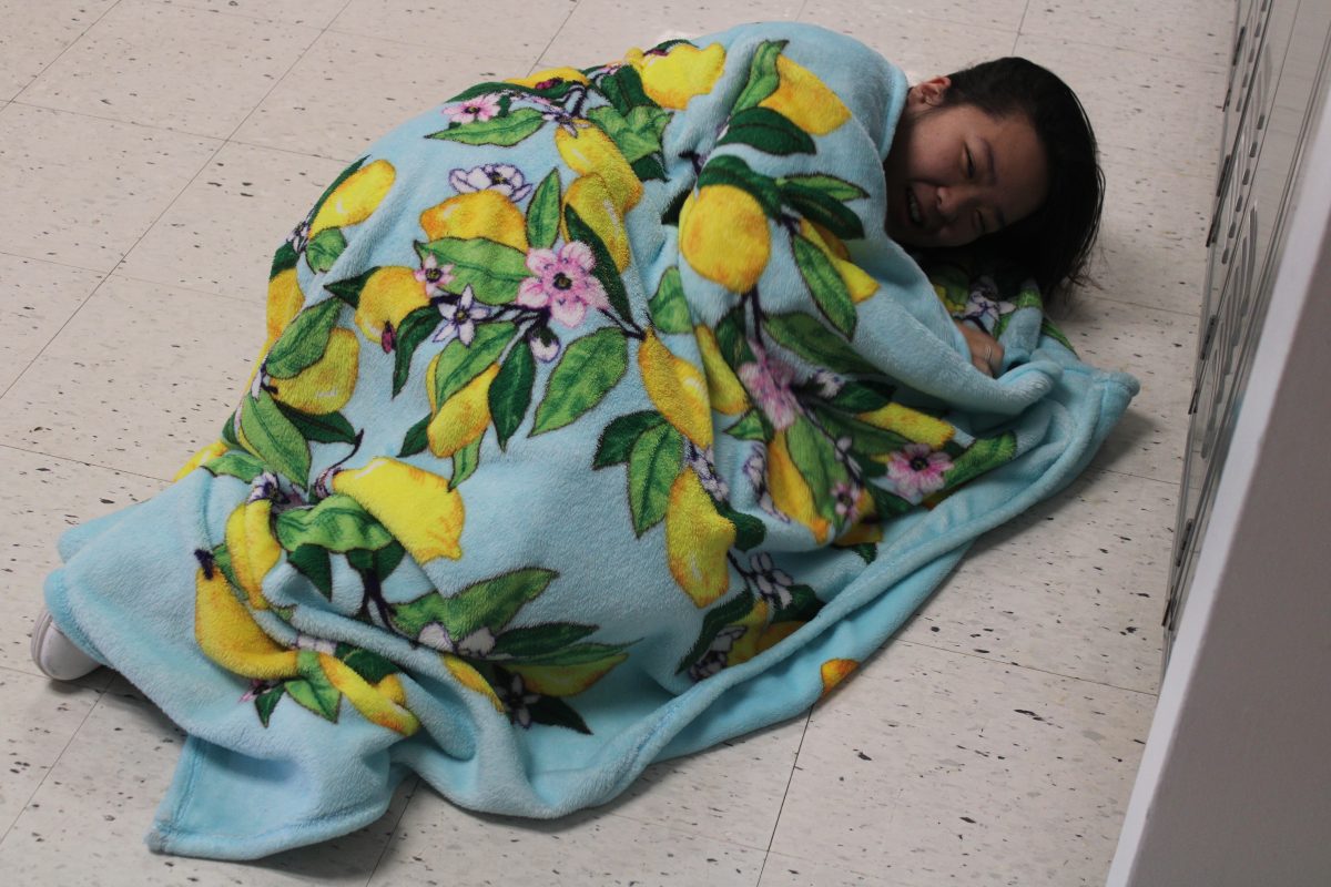 Junior Amber Zhu curls up with a blanket in the hallway.