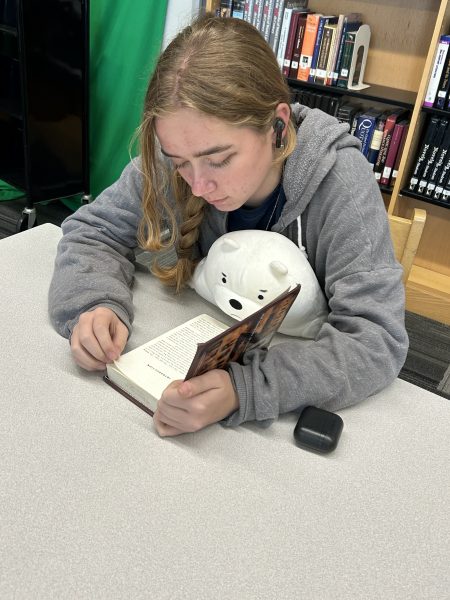 Sophomore Zoe Clark listens to music while reading to help them concentrate during lunch in the library.