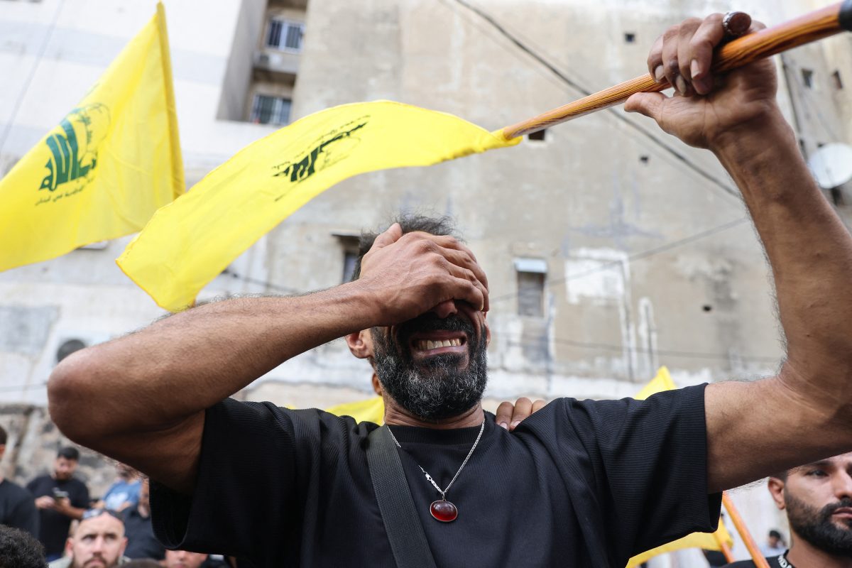 A man is crying while holding a Hezbollah flag during the funeral for people killed by an Israeli attack of exploding pagers and walkie-talkies. 